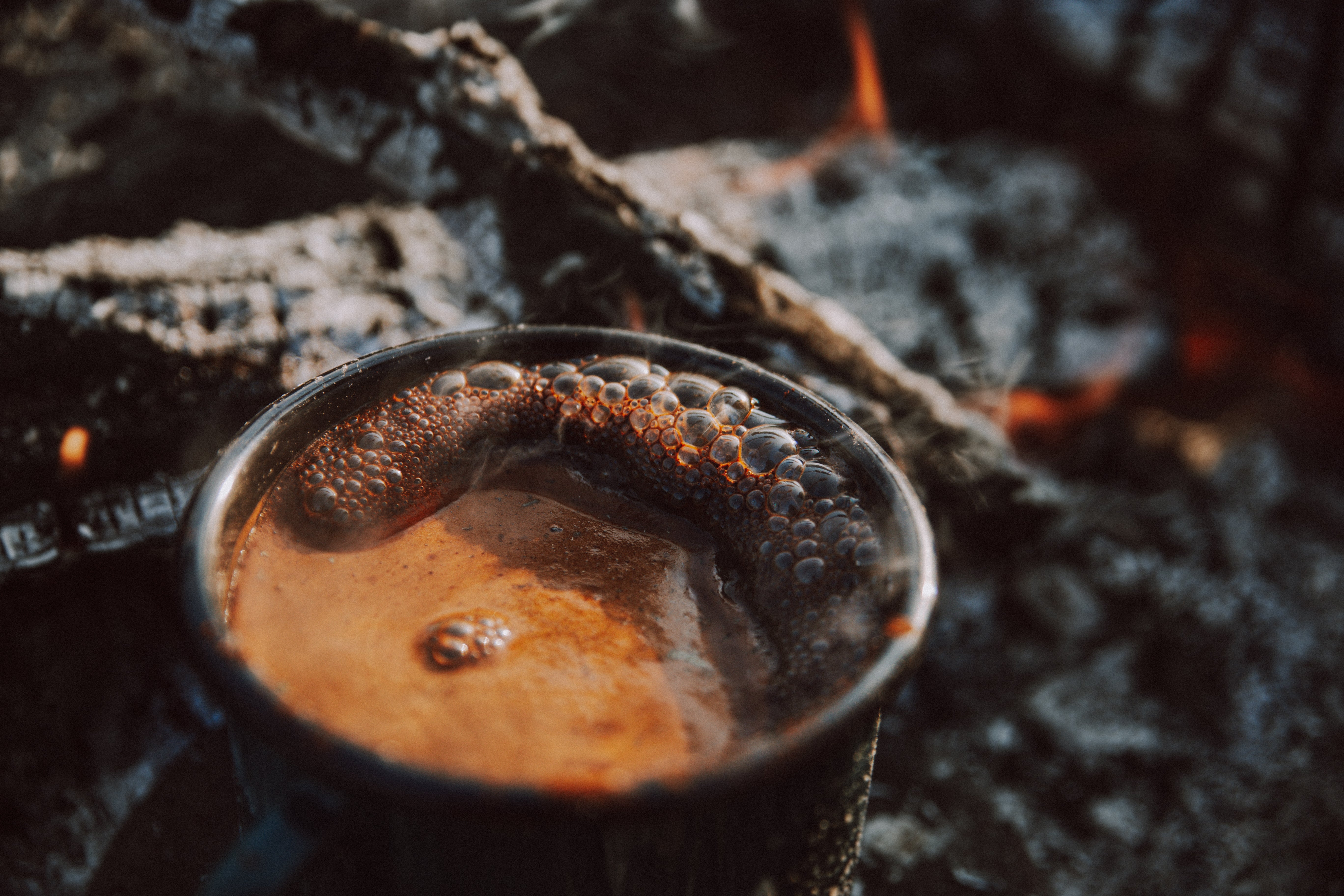 A cup of coffee beside a fire gentlty frothing