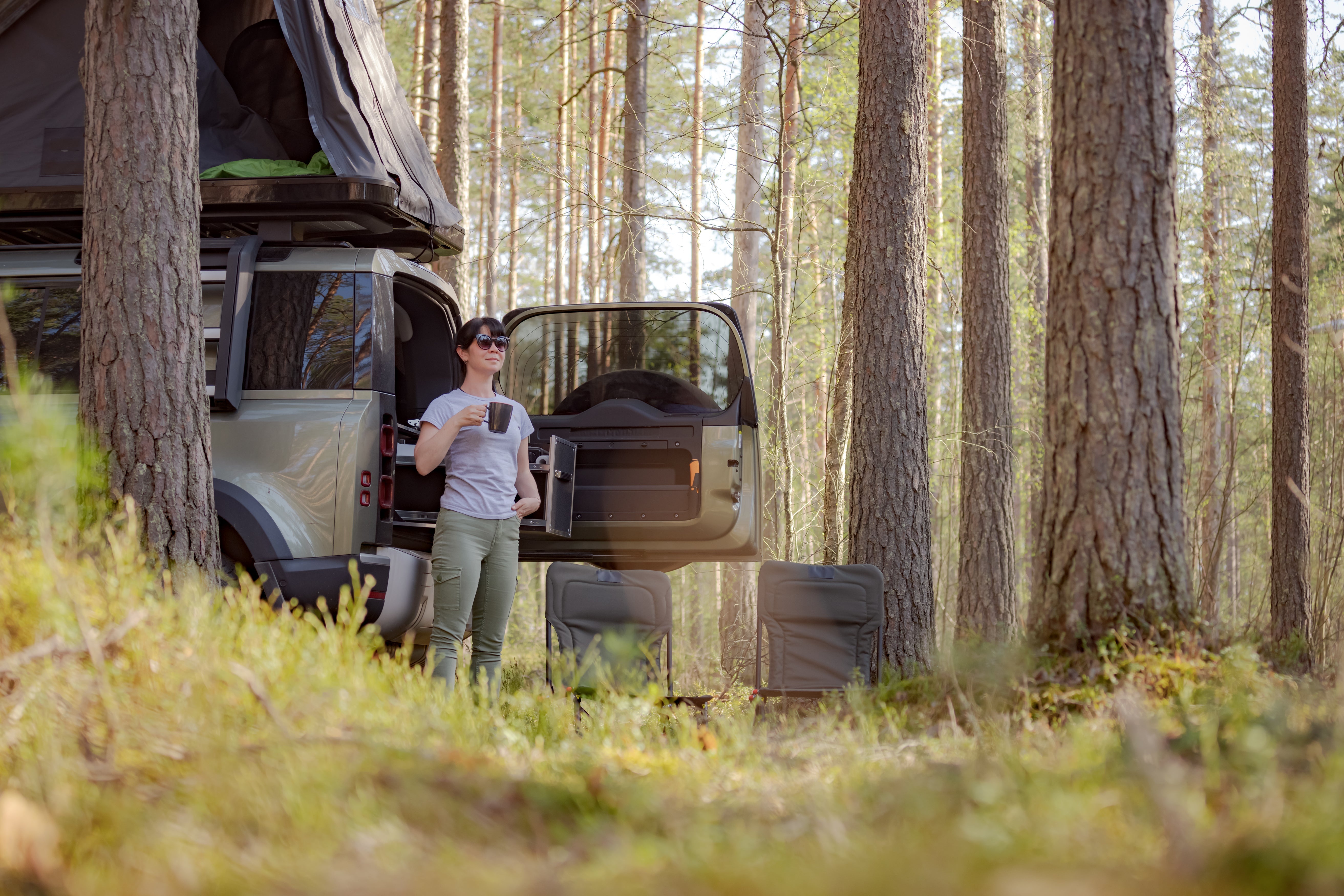 Woman standing by an overlanding vehicle enjoying a cup of coffee